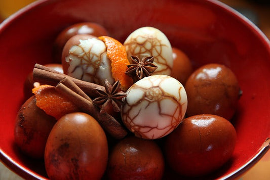 A bowl of marbled tea eggs with spices and orange peel and some eggs are peeled and others are not.