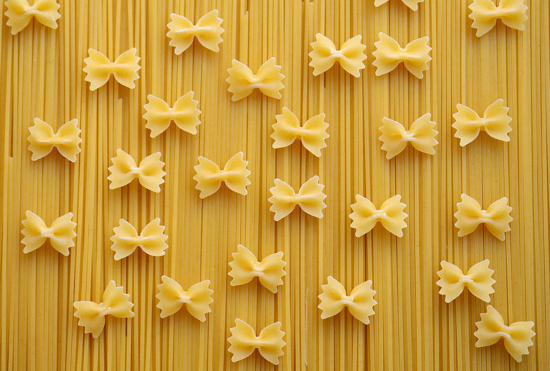 A layer of spaghetti lying vertically with scattered farfalle pasta over it