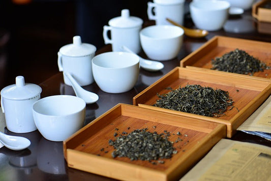 Multiple sets of white tea tastings sets with brewing cup, tasting cup, spoon and brown trays of dry tea leaves in front of them.
