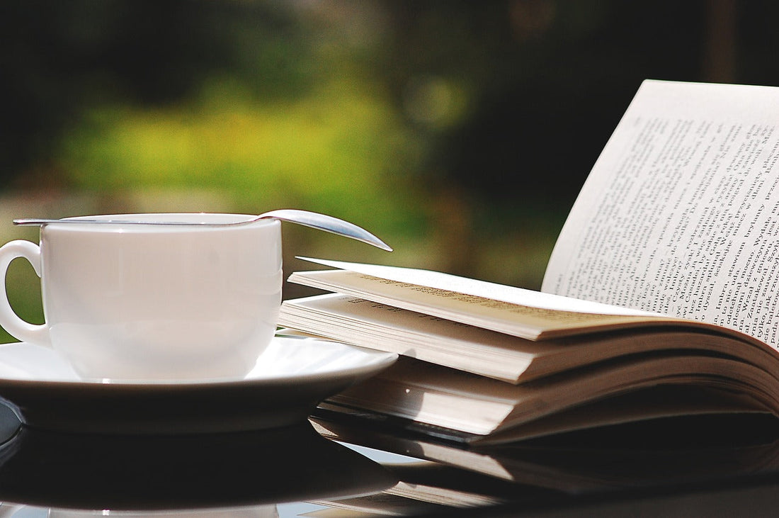 a photo of a white cup of tea/saucer with an upside down spoon setting on top next to a stack of books