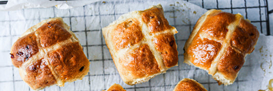 A horizontal line of hot cross buns on a wire rack.