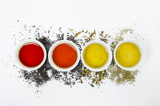 Four cups of brewed tea in different colors surrounded by scattered tea leaves