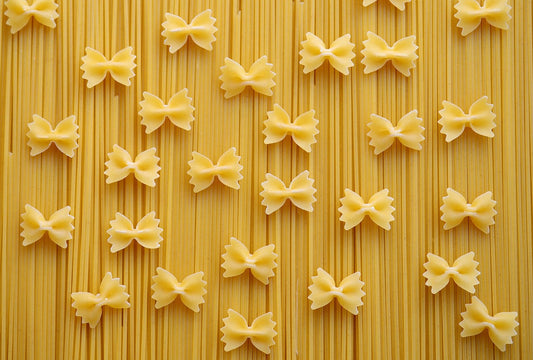 A layer of spaghetti lying vertically with scattered farfalle pasta over it 