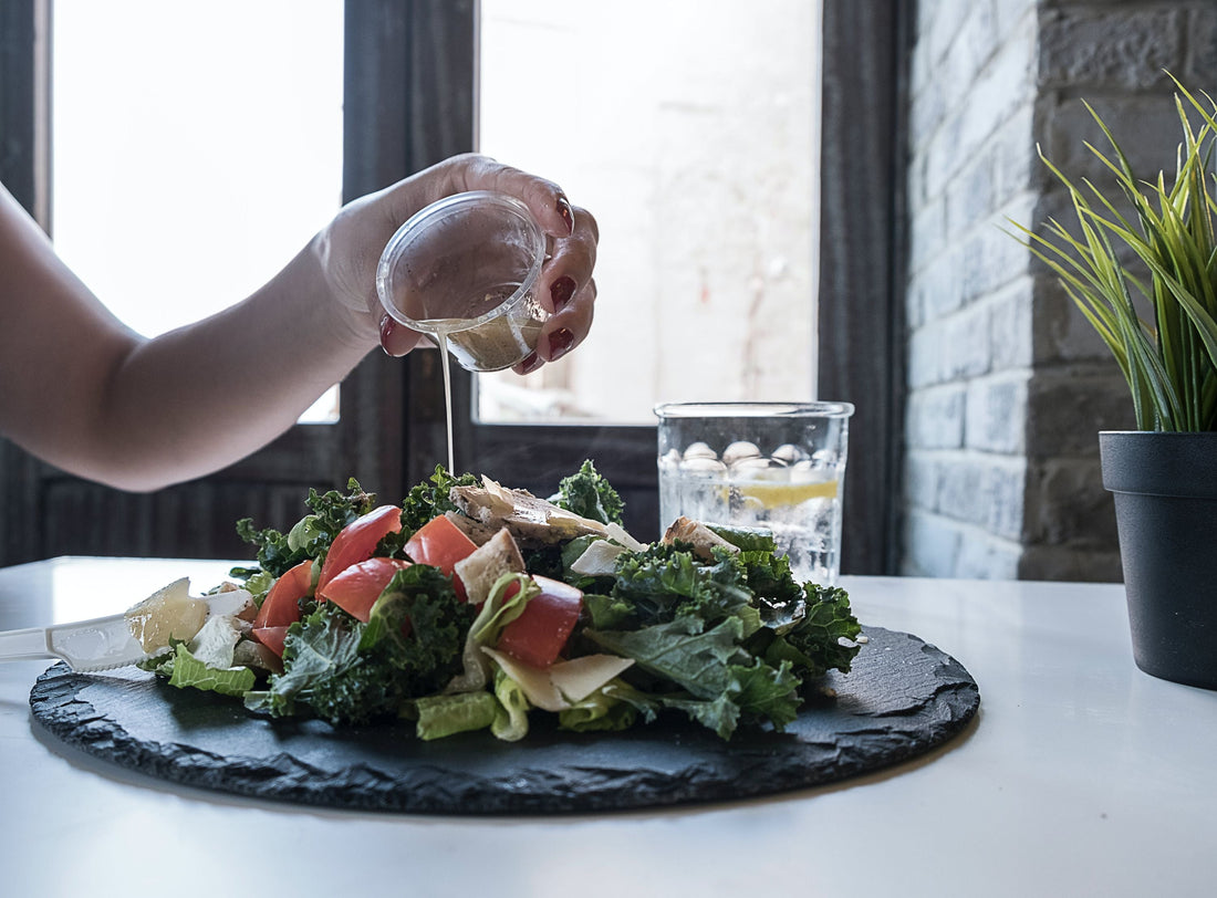 Colorful salad setting on a black plate with a person pouring over vinaigrette over it