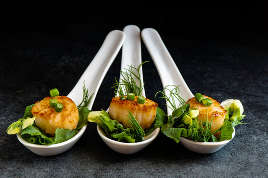3 white appetizer spoons with scallops and green garnish